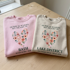 Pair of sweatshirts: pink BATH and sand LAKE DISTRICT with floral heart location text