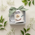 Gift box with white ceramic mug and green bow; mug text includes “EVERYTHING WILL BE OKAY”