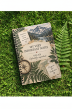Premium mockup of the Oscar notebook on grass with a fern and compass
