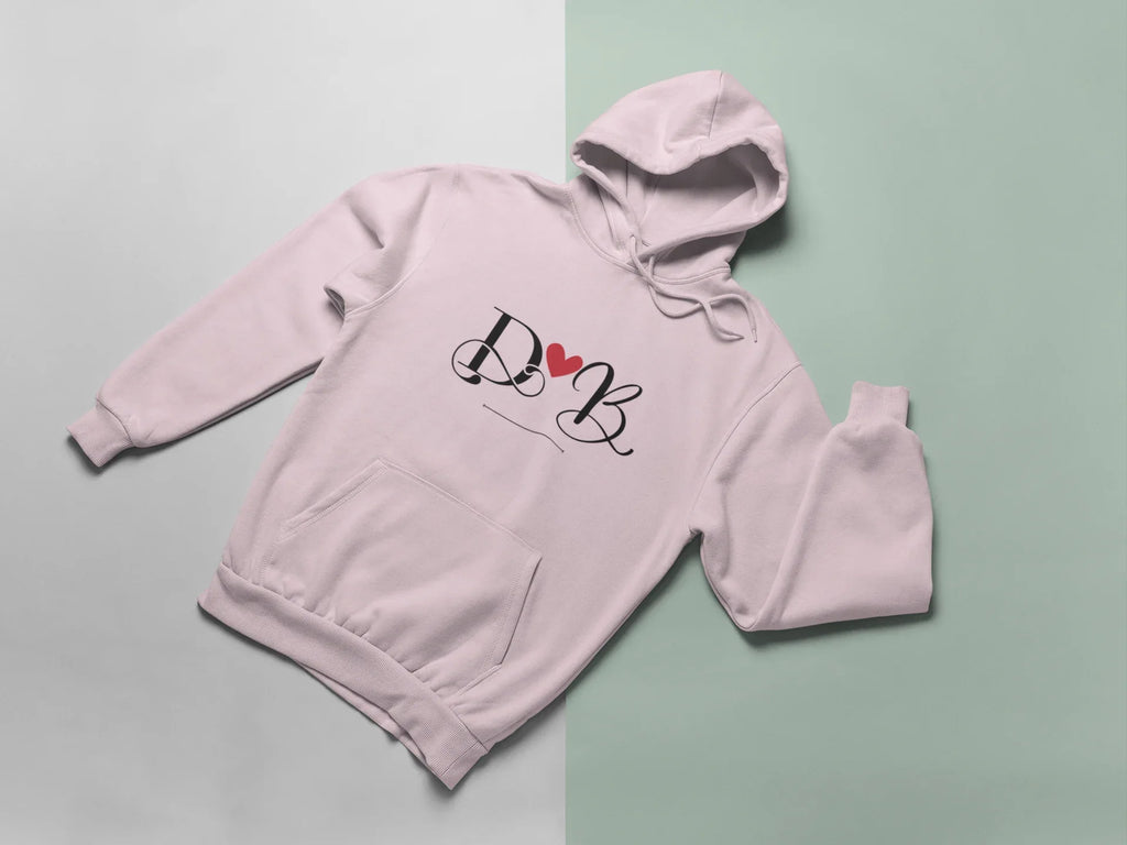 Pale pink hoodie with heart monogram graphic on chest, folded view with hood