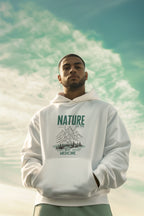 White hoodie worn by a man with green nature mountain “Best Medicine” print.