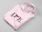 Light pink hoodie with heart monogram graphic on front, folded view