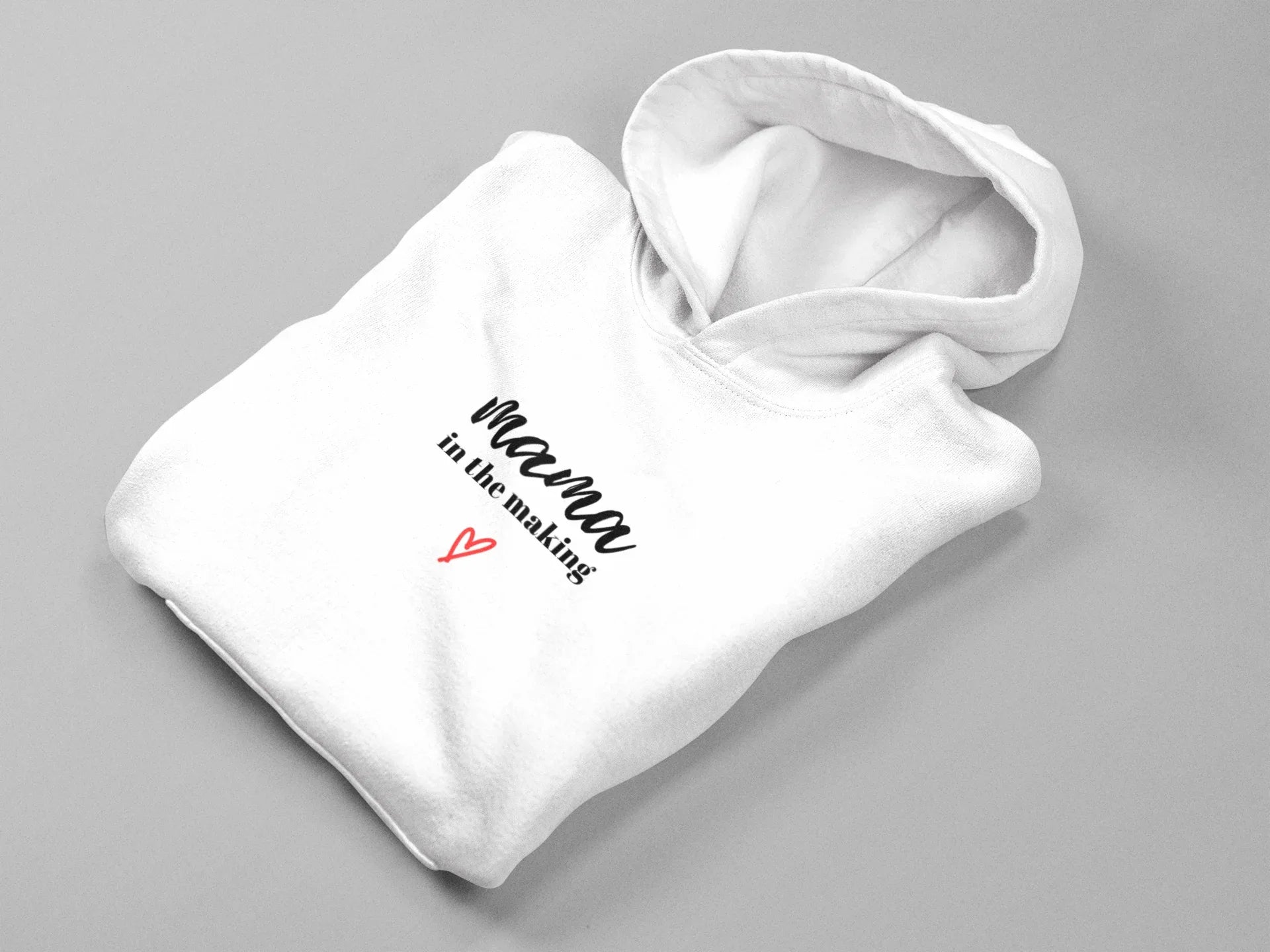 Folded white hooded sweatshirt with 'mama in the making' logo and red heart