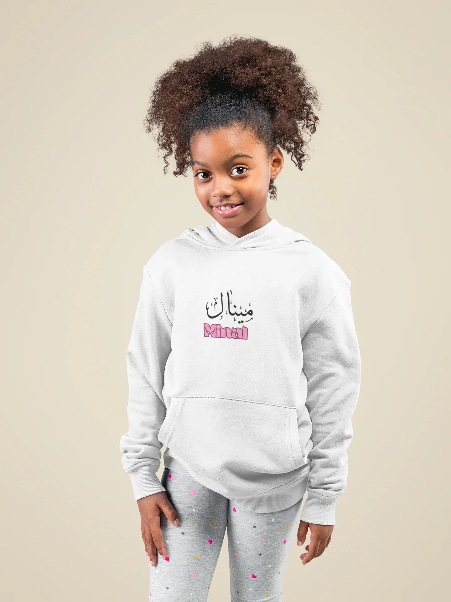 Kids white hoodie with hood and Arabic name print on chest, worn with speckled leggings.
