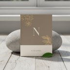 A5 notebook with taupe cover, gold monogram N, floral corner details, and spiral binding.