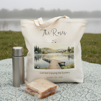 White canvas tote bag with a printed lakeside boardwalk scene and hills in the distance.
