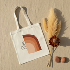 White cotton tote bag with terracotta abstract arch print and black signature on front