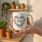 White ceramic mug held in hand with floral heart wreath and name Rosie, printed front