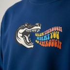 Blue sweatshirt close-up with crocodile graphic and orange multicolor “grow through” text