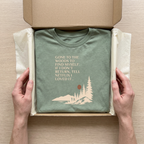 Sage green hiking t-shirt folded in shipping box with woodland graphic and quote
