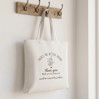 Cream tote bag hanging on wall hooks with lavender flower graphic and “than you” message