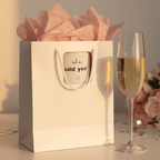 White gift bag with printed 'she said yes!' mug graphic and pink tissue.