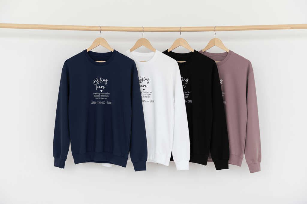 Crewneck sweatshirts on hangers in navy, white, black, sand, and mauve with 'sibling team' print