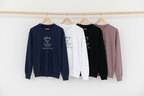 Crewneck sweatshirts on hangers in navy, white, black, sand, and mauve with 'sibling team' print