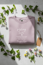Lavender crewneck sweatshirt folded with printed “sibling team” quote on front