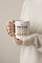 White mug held in hand, with stacked SISTER text and small heart icon