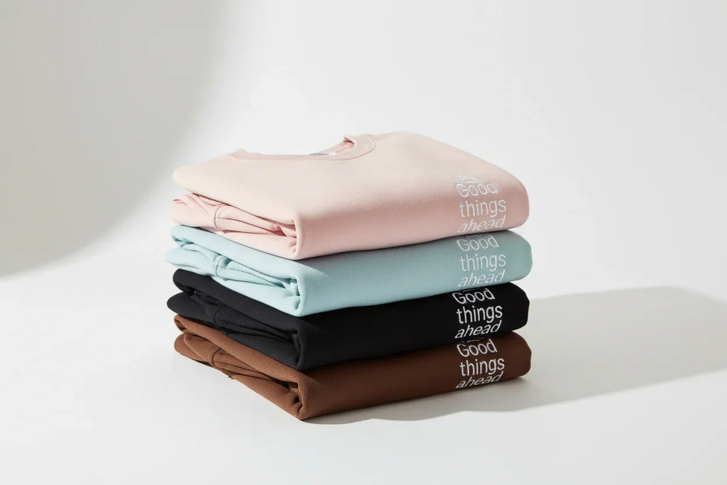 Stacked crewneck sweatshirts in blush, light blue, black, and brown
