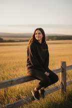 Black hoodie worn on grass field, with small chest logo text.
