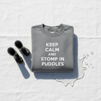 Light gray crewneck sweatshirt with white text: KEEP CALM AND STOMP IN PUDDLES
