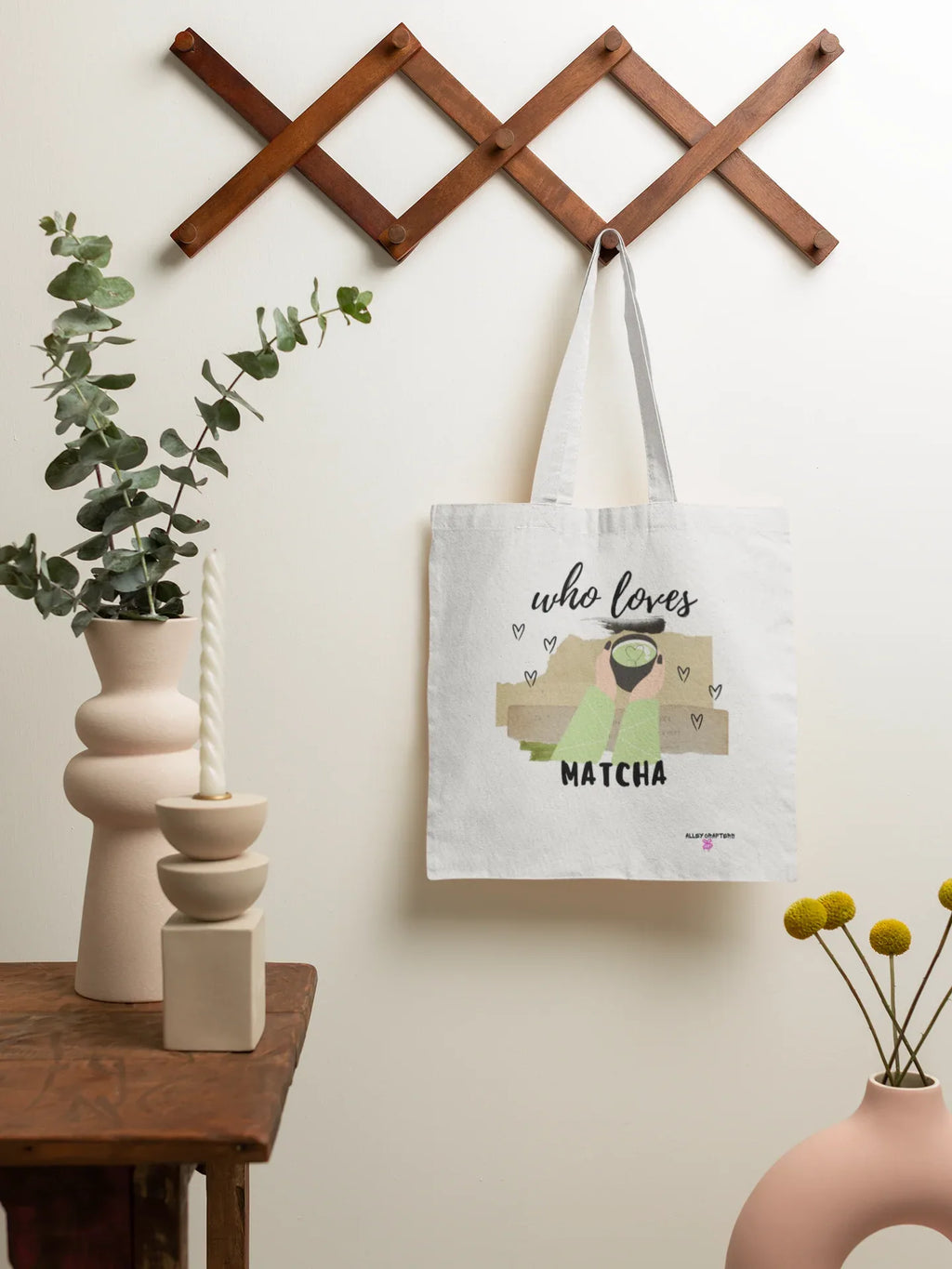 White tote bag hanging on wall hook, featuring “who loves MATCHA” illustration.