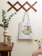 White tote bag hanging on wall hook, featuring “who loves MATCHA” illustration.