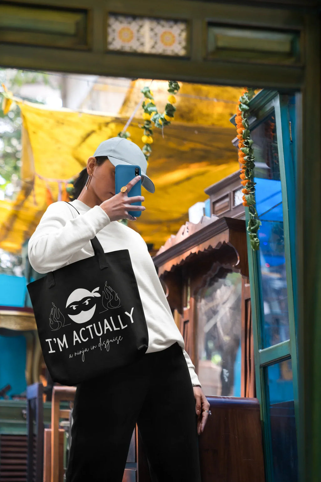 Black tote bag worn on shoulder with ninja face logo and 'I'M ACTUALLY' text.