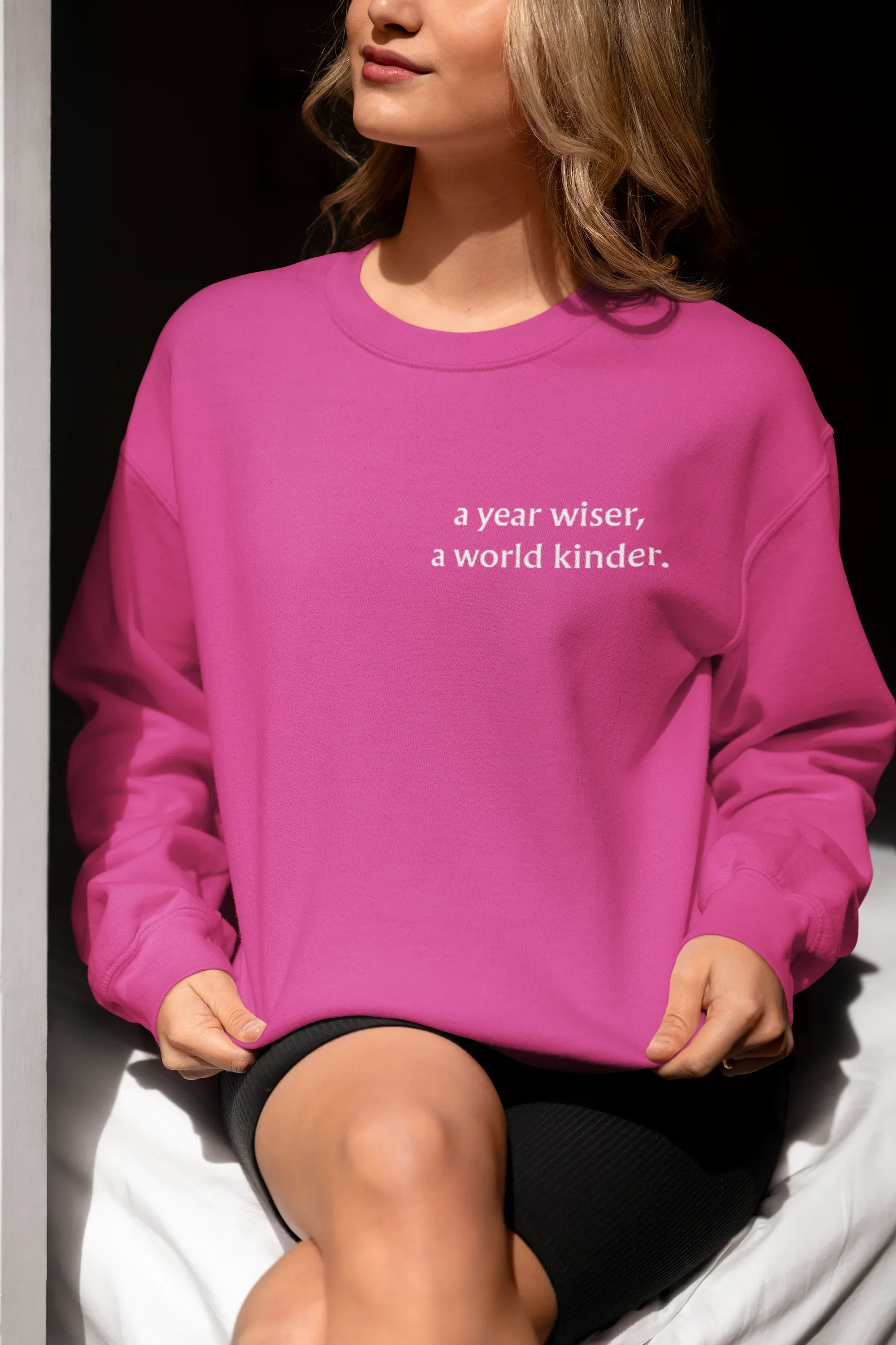 Pink crewneck sweatshirt with 'a year wiser, a world kinder.' print