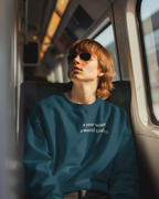 Teal crewneck sweatshirt with chest text: "a year wiser, a world kinder"