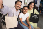 Black canvas tote bag with “Best Mum ever” white print, held by woman in group photo