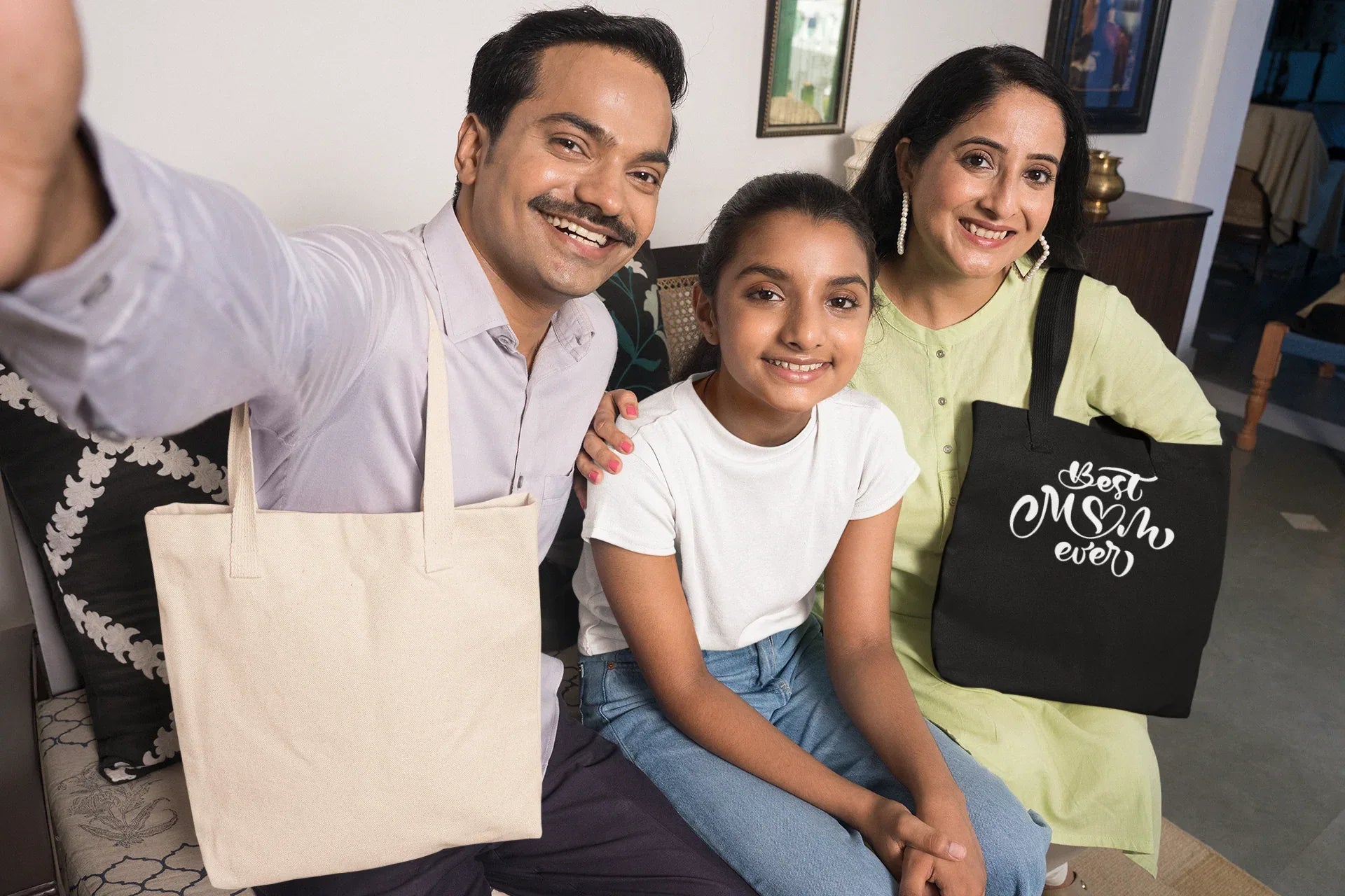 Black canvas tote bag with “Best Mum ever” white print, held by woman in group photo