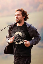 Black graphic T-shirt with mountain sunrise “RISE ABOVE” worn with jacket