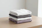 Stack of folded crewneck sweatshirts in white, dark gray, and lavender with chest text