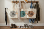 White cotton tote bags with circular name prints, hanging on hooks