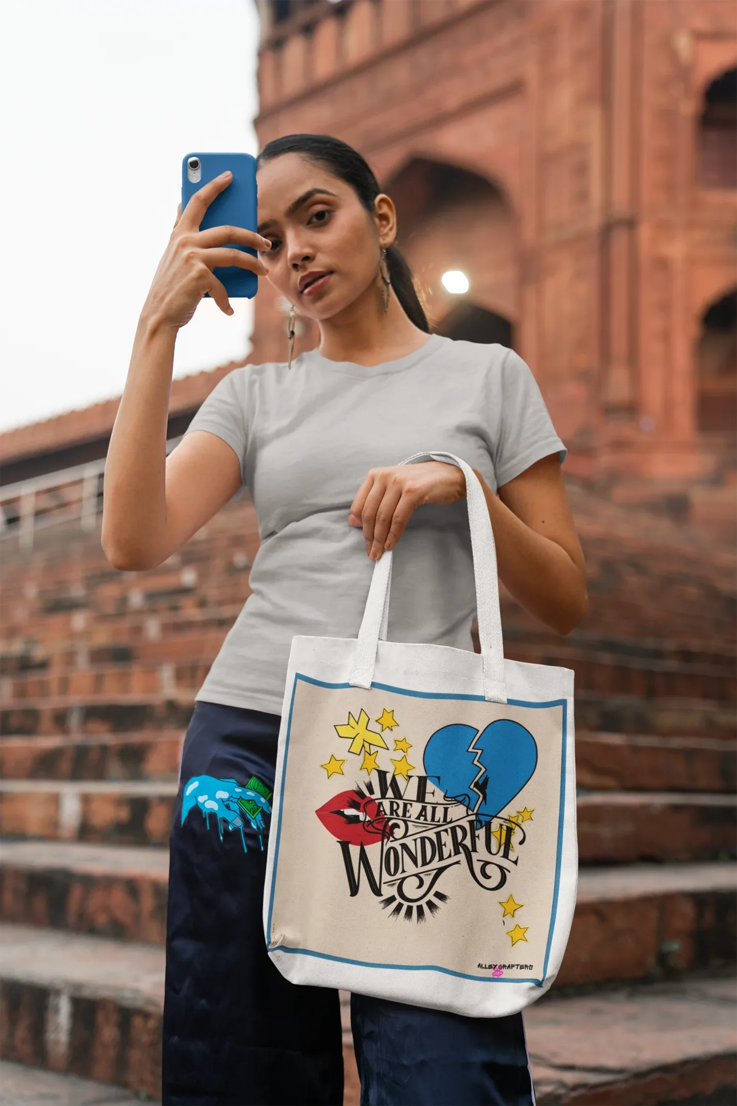 White canvas tote bag with blue-bordered front graphic and black shoulder straps