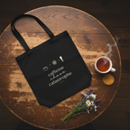 Black tote bag with coffee graphic and icons, shown with a cup nearby