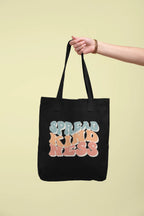 Black cotton tote bag with 'SPREAD KINDNESS' graphic, held by a hand