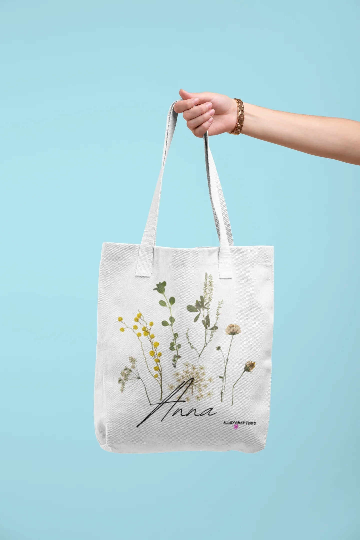 White canvas tote bag with light handle straps and botanical flower print, cursive "Anna"