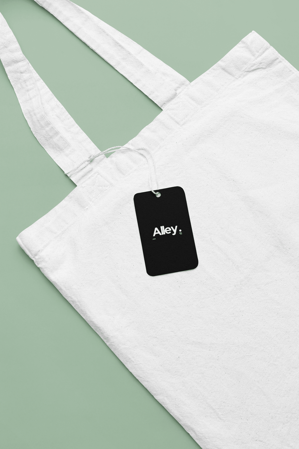White canvas tote bag with black hanging tag reading Alley.