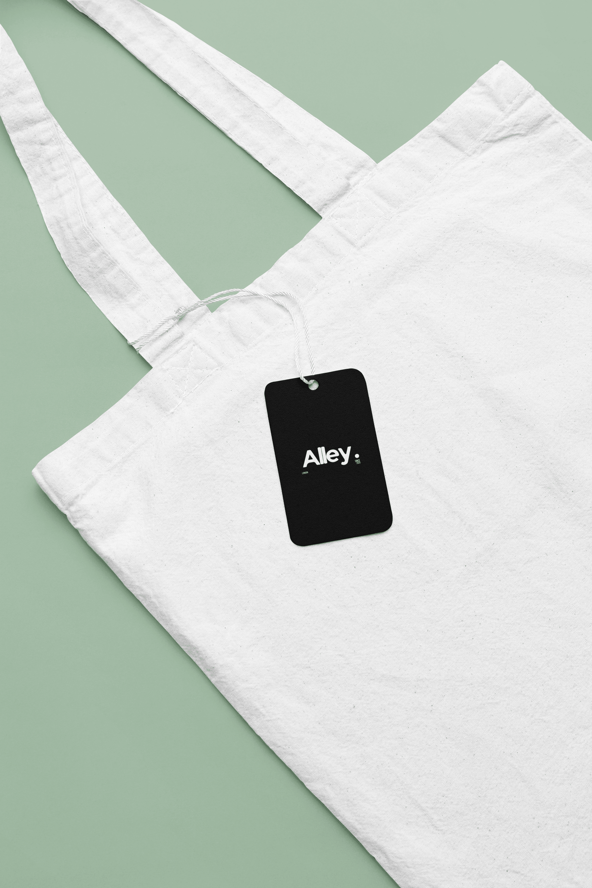 White canvas tote bag with black hanging tag reading Alley.
