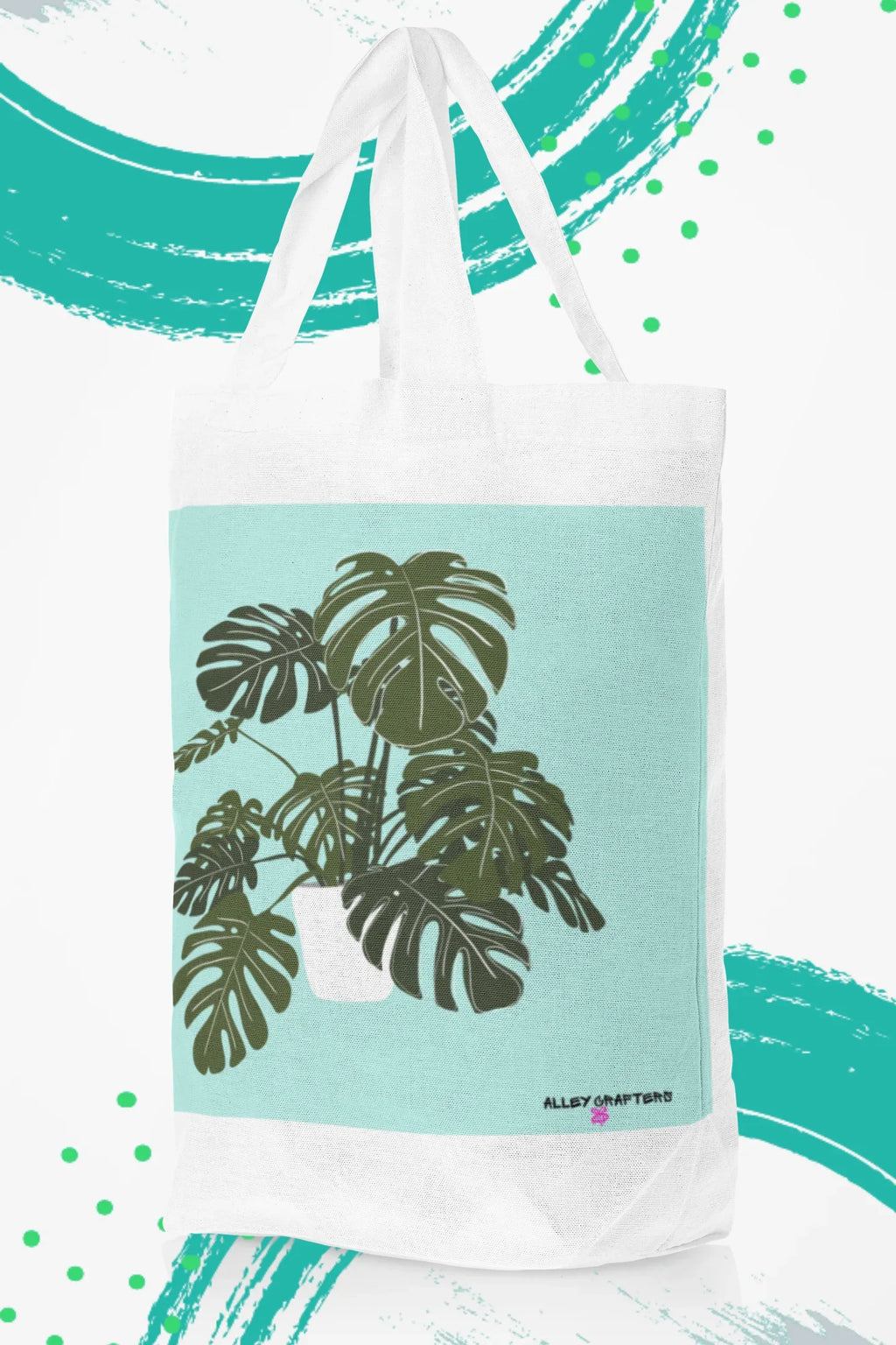 White tote bag with black handles and green monstera leaf print on teal panel