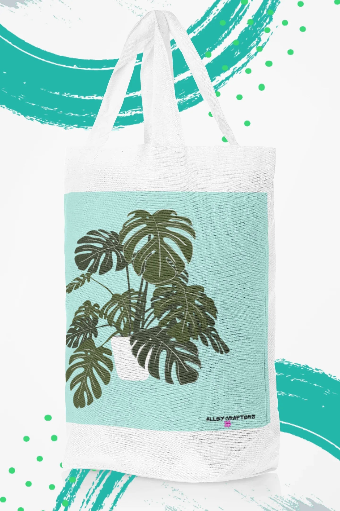 White tote bag with black handles and green monstera leaf print on teal panel