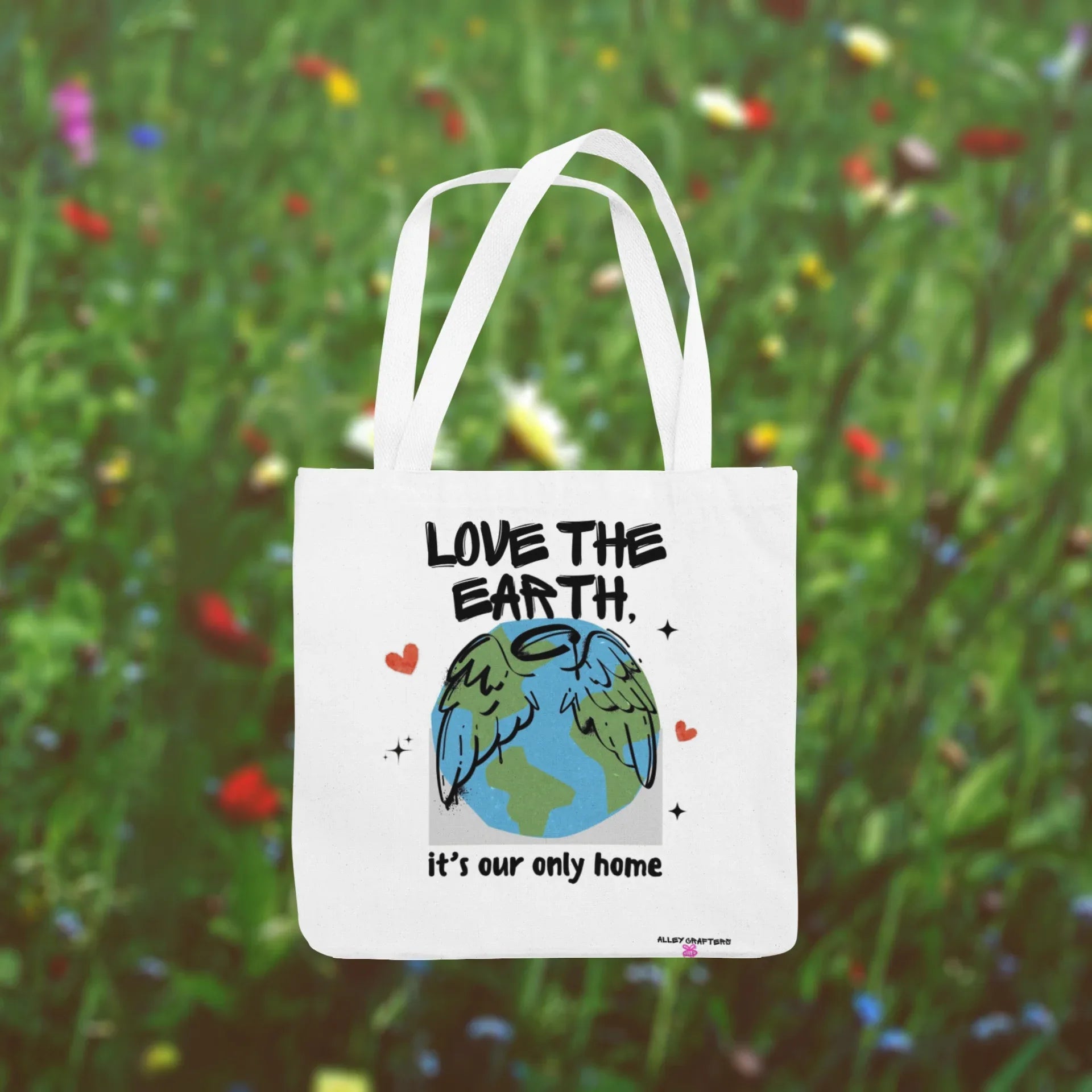 White tote bag with “Love the Earth” text and globe illustration in garden