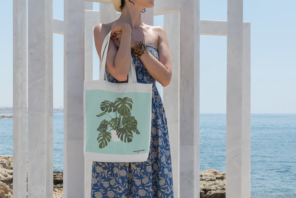 White tote bag with black handles and green monstera print, held in front