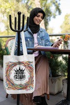 White tote bag in use, featuring black crown emblem and multicolor scribble wreath