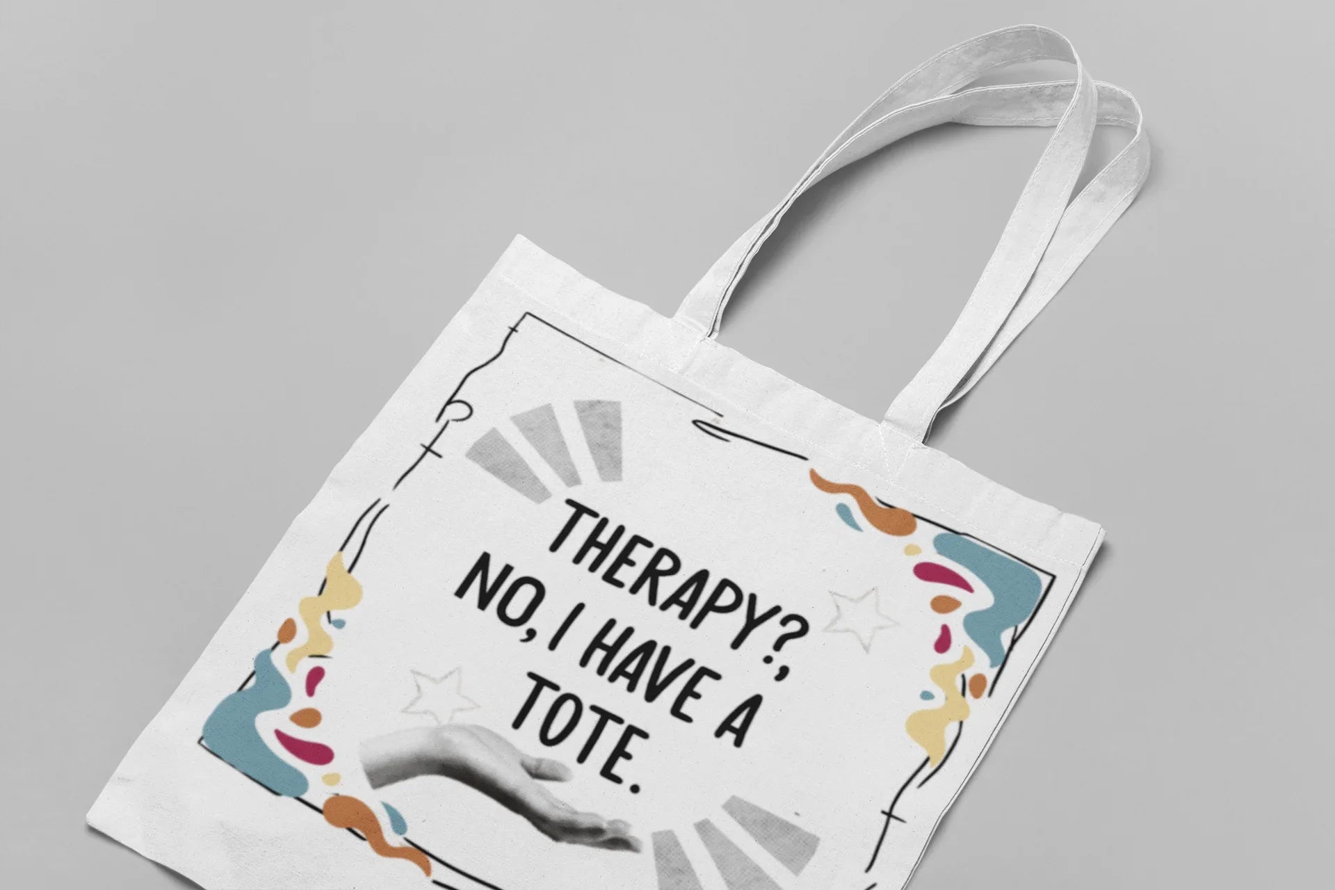 White tote bag with printed quote and colorful border, shown from above with handles.