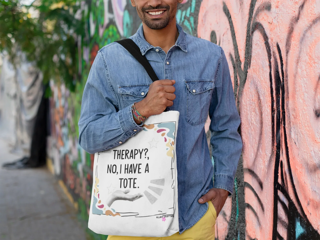 White tote bag with printed quote and colorful doodles, worn over denim shirt.