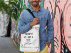 White tote bag with printed quote and colorful doodles, worn over denim shirt.