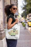 White tote bag with “who loves MATCHA” illustration and heart details, over-the-shoulder.