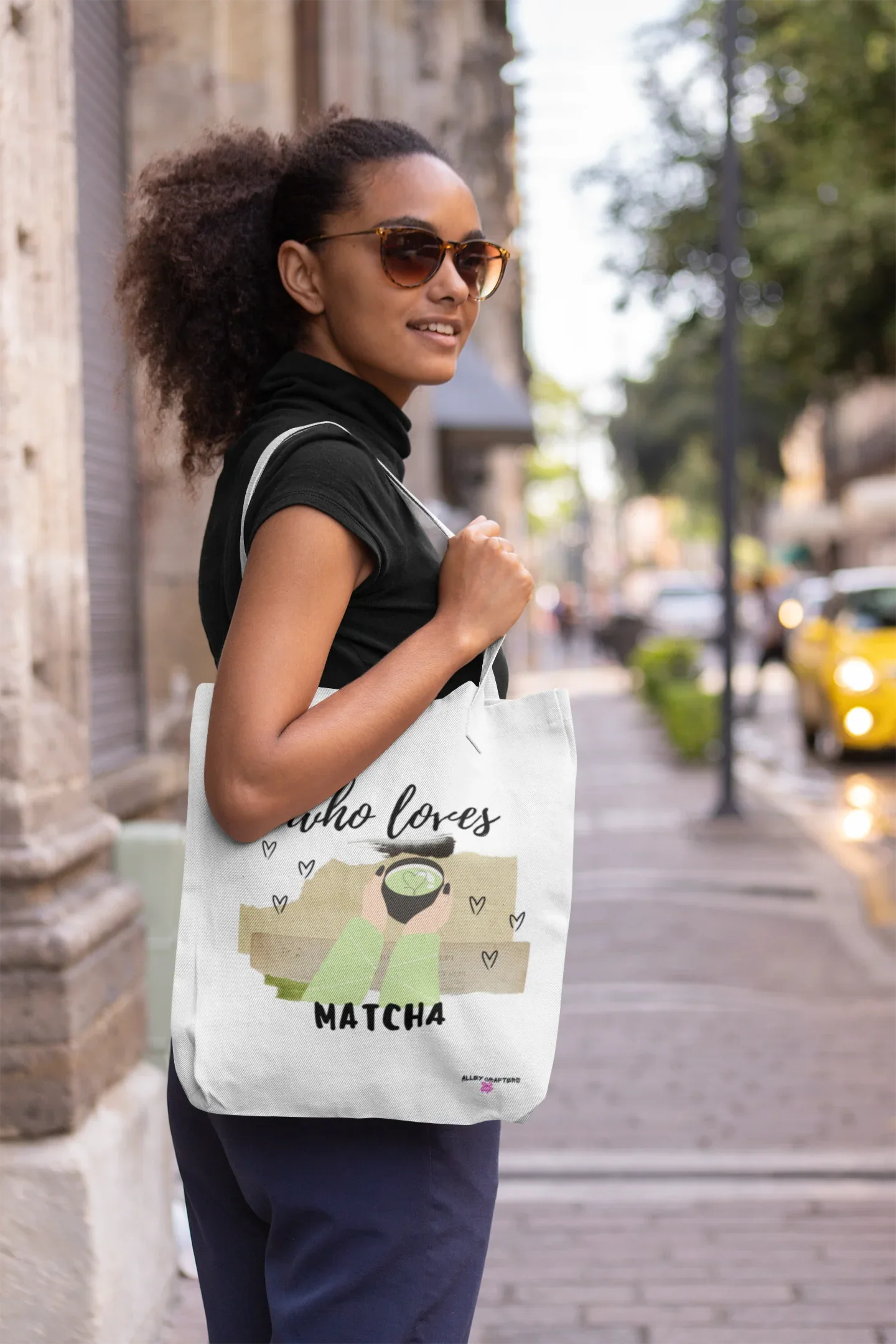 White tote bag with “who loves MATCHA” illustration and heart details, over-the-shoulder.