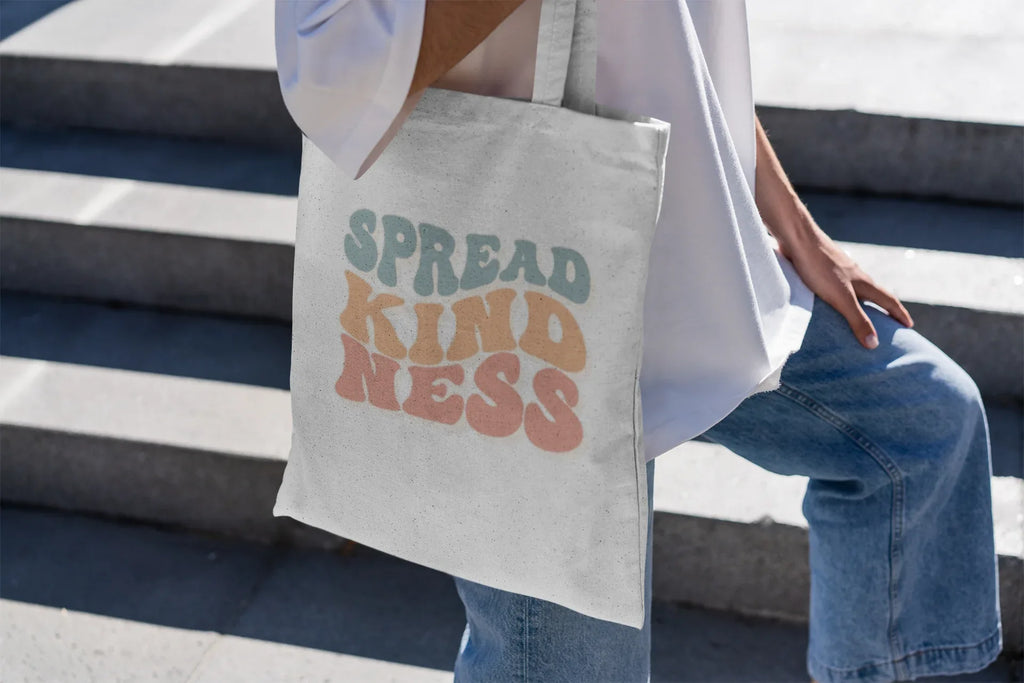 Light gray cotton tote bag with 'SPREAD KINDNESS' graphic, held by a person